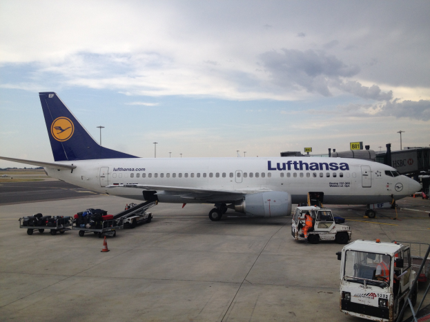 Lufthansa Airbus A320-200-Flugzeug am Frankfurter Flughafen geparkt mit Bodenbetriebsfahrzeugen, Verkehrskegeln und Informationsschildern im Hintergrund unter einem bewölkten Himmel.
