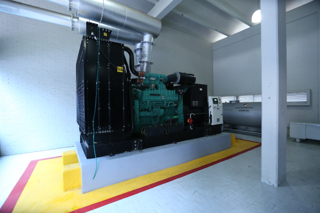 Ein großer Dieselmotor in einem Raum mit Boden, Säule, Wand, Deckenleuchten und anderen Gegenständen.