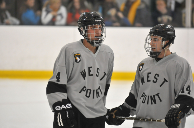 Zwei Hockey-Spieler in Helm und Handschuhen stehen auf einem Eisstadion und halten Hockey-Schläger.