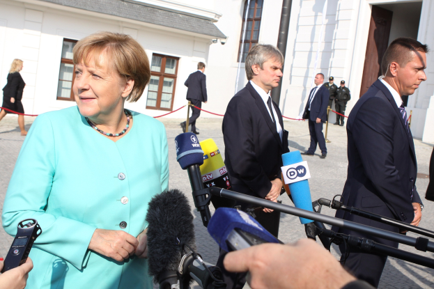 Bundeskanzlerin Angela Merkel spricht mit Reportern vor dem Bundeskanzleramt in Berlin, umgeben von einer Gruppe von Menschen, einige halten Mikrofone, mit Gebäuden im Hintergrund.