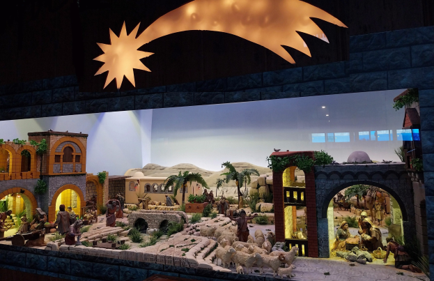 Eine Krippe in einem Museum mit Figuren, Tieren, Gebäuden und Grünpflanzen, beleuchtet von oben.