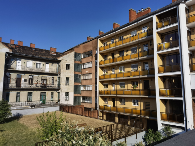 Wohnblock mit Innenhof, der von grünem Gras, Pflanzen, Bäumen und einem sichtbaren Himmel umgeben ist.