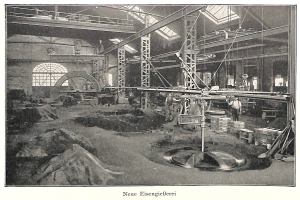 Ein altes Schwarz-Weiß-Foto einer Fabrik mit Arbeitern, die eine Maschine bedienen, umgeben von Metallstangen und -pfählen, mit der Beschriftung "Neue Eisenglebeerei, die erste Fabrik in Deutschland" unten.