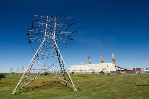 Elektromasten, Kabel, Gebäude mit Schornsteinen, Bäume und ein bewölkter Himmel.