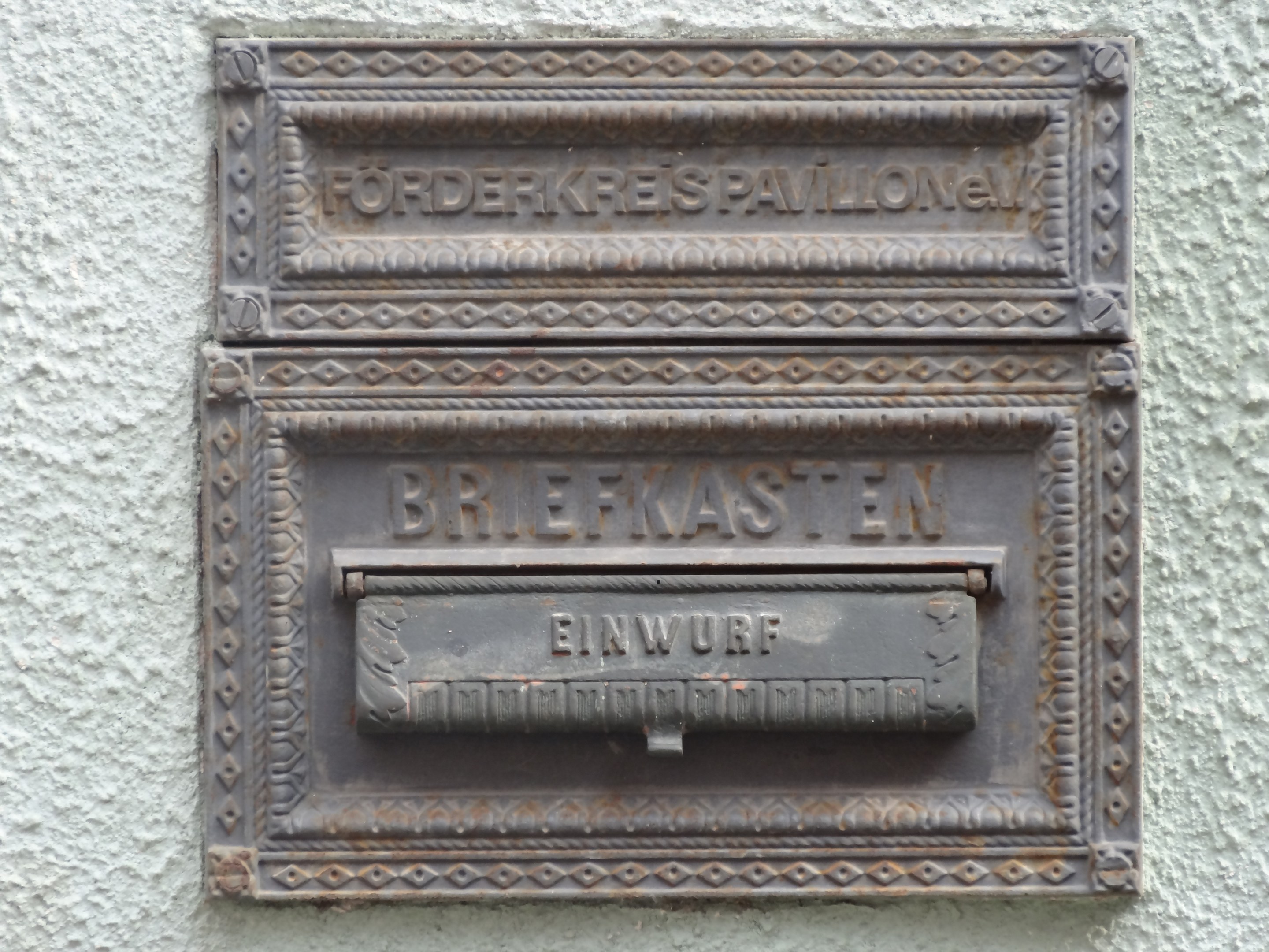 Alter rechteckiger Metallbriefkasten mit einem oberen Griff, an einem Gebäude montiert, beschriftet mit "Briefkasten" in schwarzer Schrift.