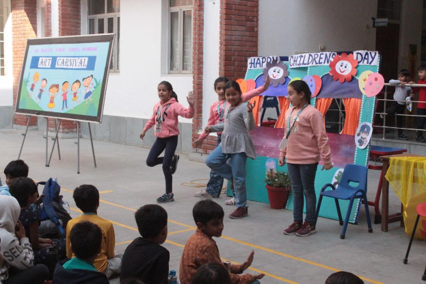 Eine Gruppe von Kindern sitzt vor einem Gebäude auf dem Boden und hält ein Schild in die Höhe, während sie an einem Kinderfest teilnehmen.