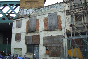 Ein Hausaufbau in der Mitte, Fahrzeuge unten, ein Pfahl links, eine Brücke oben und ein hölzerner Bambusaufbau rechts.