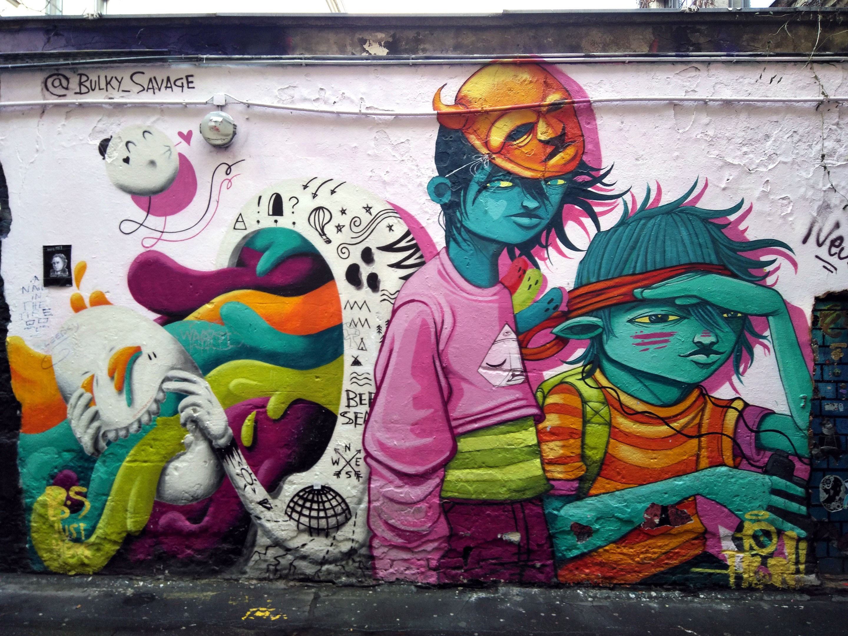 Mural an der Seite eines Gebäudes mit Graffiti, das eine Straße am Boden, Strommasten und einen klaren blauen Himmel im Hintergrund zeigt.