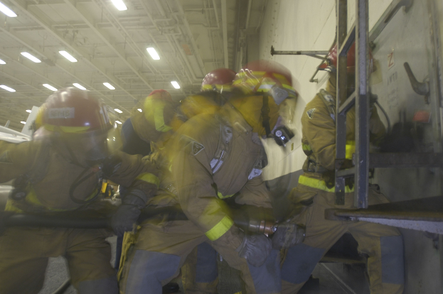 Feuerwehrleute in Schutzausrüstung arbeiten an einem Flugzeug mit einer Leiter auf der rechten Seite, was auf eine Notfallreaktion hinweist.