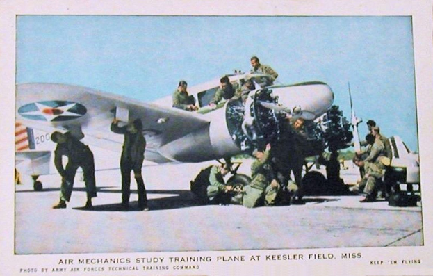 Gruppe von Menschen um ein Trainingsflugzeug auf einer Landebahn mit einem klaren blauen Himmel im Hintergrund und dem Text "Luftmechaniker-Studium Trainingsflugzeug auf Keesler Field, Miss." unten.