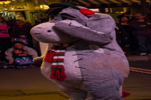 Eine Person in einem Tierkostüm steht vor einer Menschenmenge, mit Lichtern auf dem Dach.