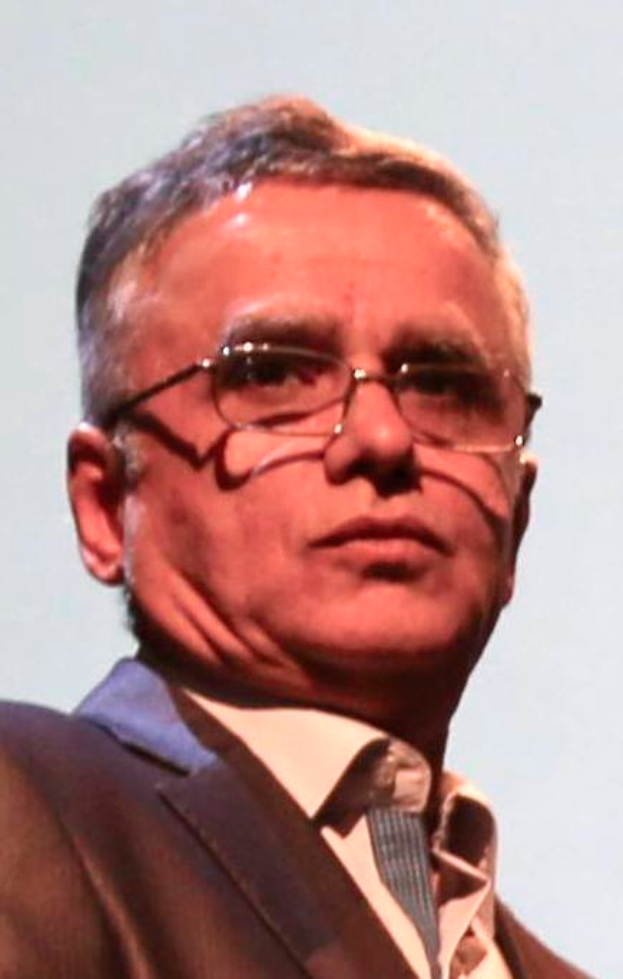 Ein Mann in Blazer, Krawatte und Brille steht vor einem weißen Hintergrund, identifiziert als Chief Executive Officer der Bank of England.