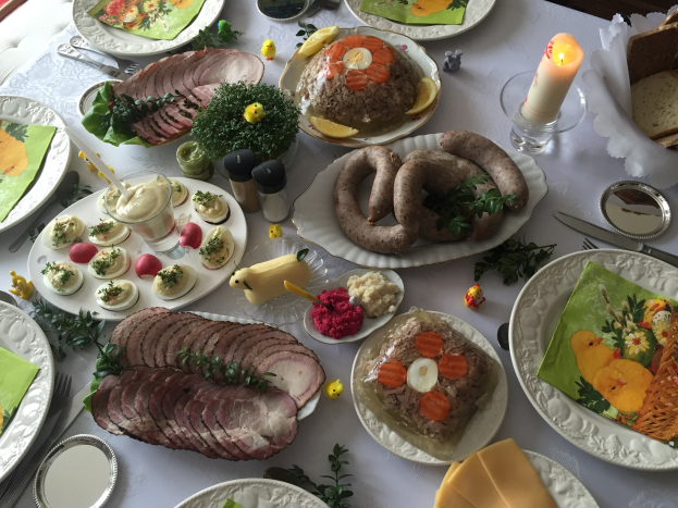 Ein für ein traditionelles deutsches Osteressen gedeckter Tisch mit verschiedenen Gerichten, Besteck und Stühlen drumherum.
