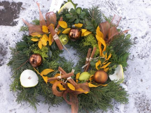 Ein festlicher Adventskranz aus Blättern, Früchten und Schmuck liegt auf schneebedeckter Erde.