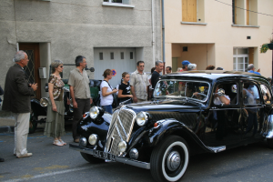Ein Auto fährt auf einer Straße mit Menschen auf der linken Seite und Gebäuden im Hintergrund.