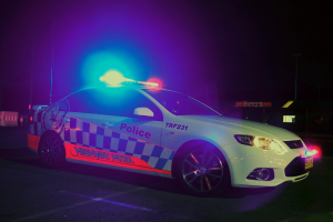 Ein weißer Polizeiwagen mit Lichtern und Aufklebern vor einem schwarzen Hintergrund.
