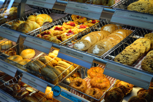 Ein Bäckereischaufenster voller verschiedener Kuchen, Kekse, Plätzchen und andere Backwaren, mit Schildern, die die Art der Backwaren angeben.