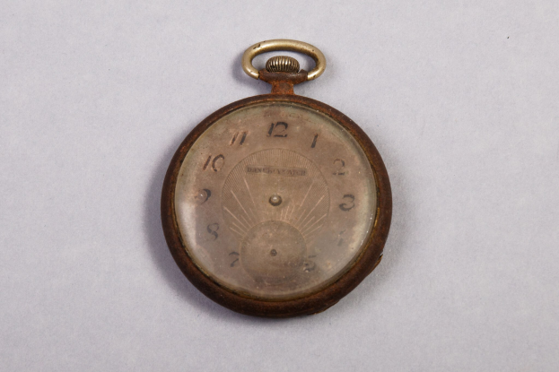 Eine klassische Taschenuhr mit einer nummerierten Zifferblatte, das auf einer weißen Oberfläche ruht.