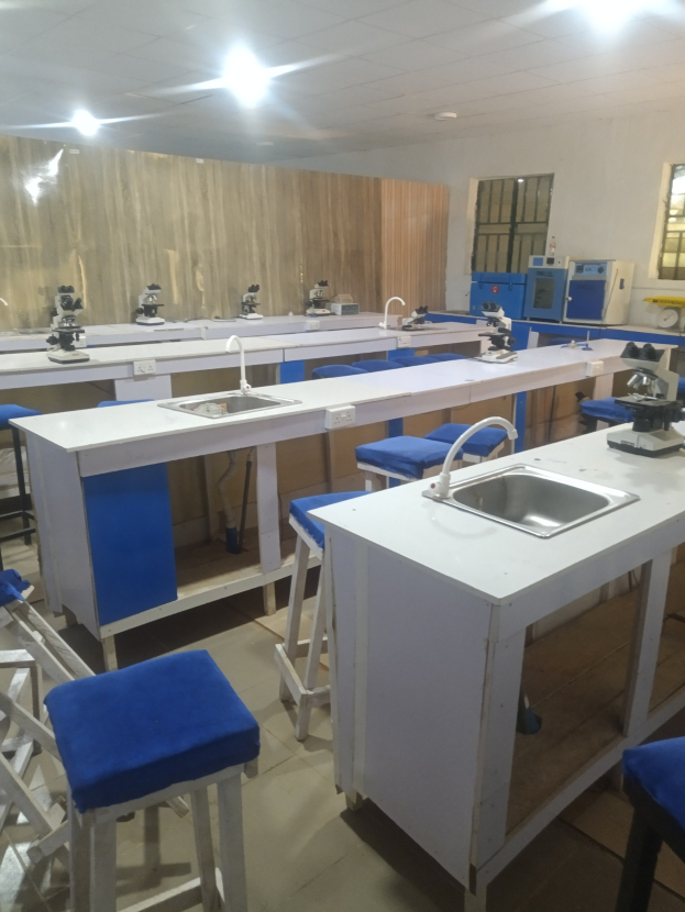 Ein Labor mit blauen Hockern, weißen Arbeitsplatten, einem Spülbecken mit Wasserhähnen, Maschinen, Fenstern an einer Wand und Deckenleuchten an der Universität für Wissenschaft und Technologie in Ahmedabad.