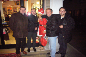 Personen, die in einem Raum mit einer Santa-Claus-Puppe, Haustiergläsern, Vorhängen, Wandbehängen, Dekolichter und Papieren stehen und sitzen.