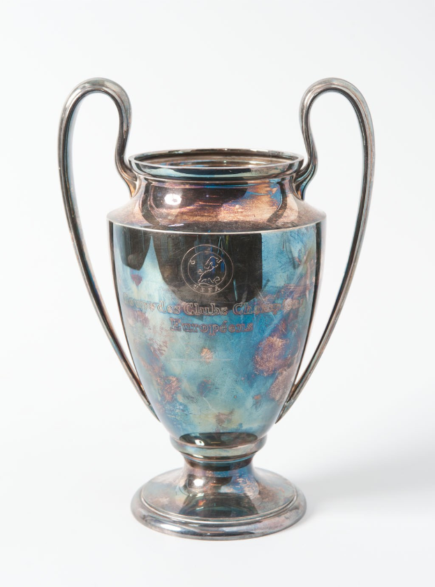 Der UEFA-Champions-League-Pokal, ein stählerner Becher mit zwei Griffen und einem blauen und silbernen Farbschema, der mit "UEFA Champions League" beschriftet ist, vor einem weißen Hintergrund.