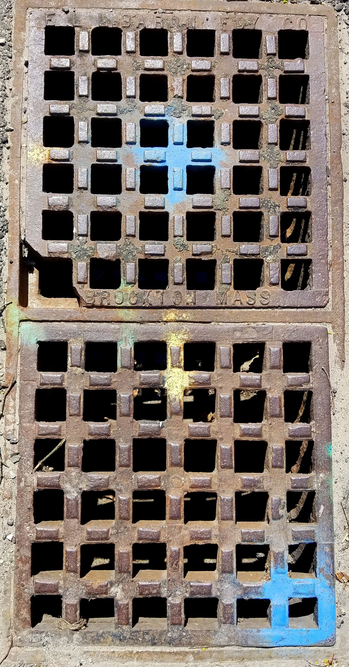 Metallschachtdeckel mit Gittermuster an der Seite eines Gebäudes.