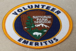 Runder Patch mit blauem Rand und weißem Hintergrund, mit fetter schwarzer Schrift "Volunteer National Park Service Emeritus" in der Mitte eines gelben Kreises.