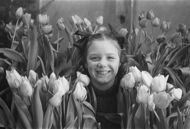 Schwarz-weiß-Foto eines jungen Mädchens, das in einem Tulpenfeld lächelt.