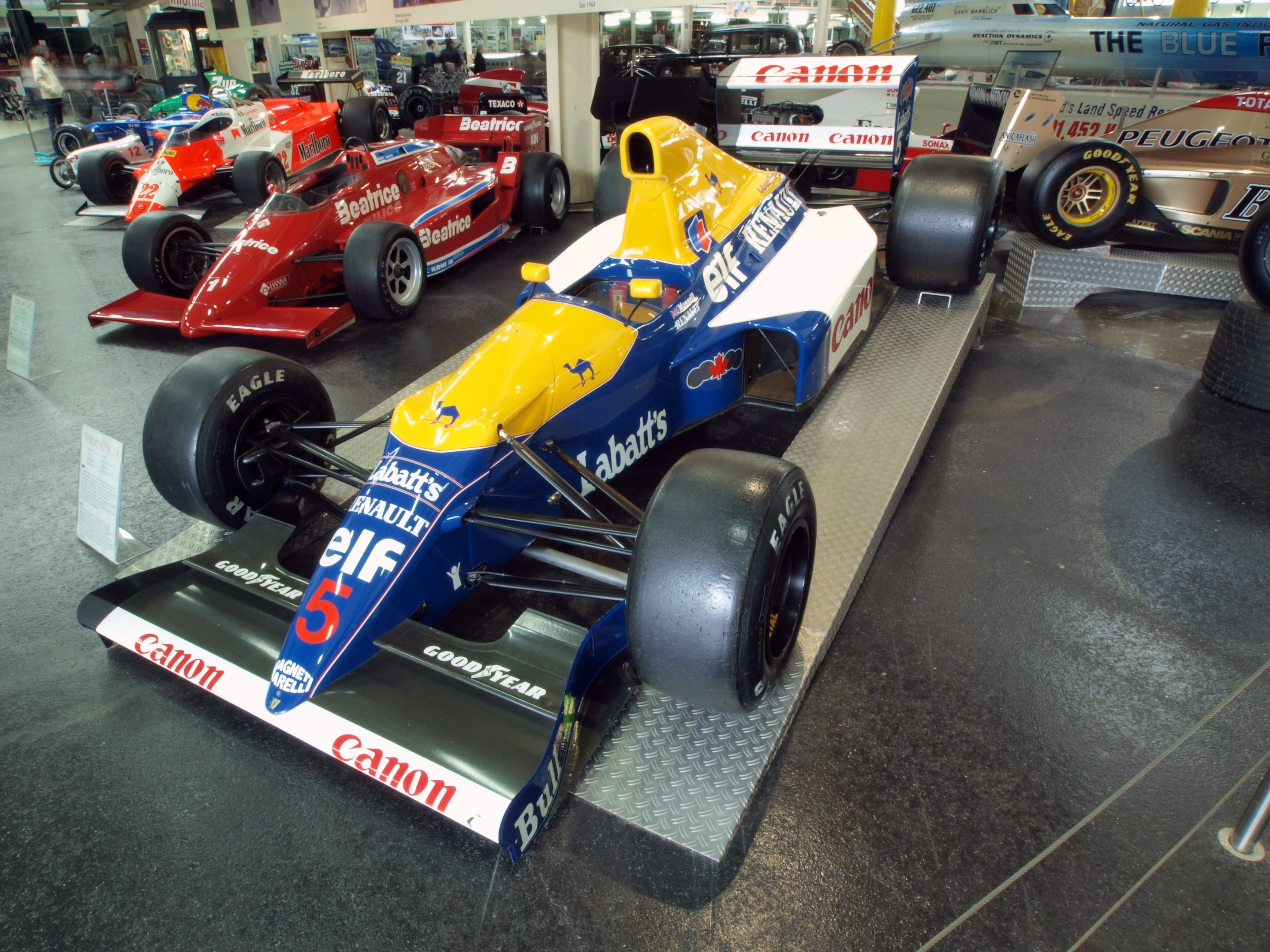 Eine Gruppe von Rennwagen in einem Museum ausgestellt, umgeben von Menschen.