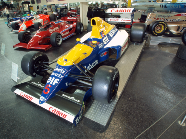 Eine Gruppe von Rennwagen in einem Museum ausgestellt, umgeben von Menschen.