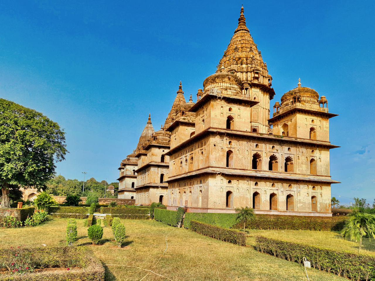 Ein großes Gebäude inmitten einer üppigen grünen Wiese umgeben von Bäumen und Pflanzen, mit einem klaren Himmel im Hintergrund und einem Wasserzeichen, das darauf hinweist, dass es eine Darstellung der besten Orte zum Besuch in Indien ist.