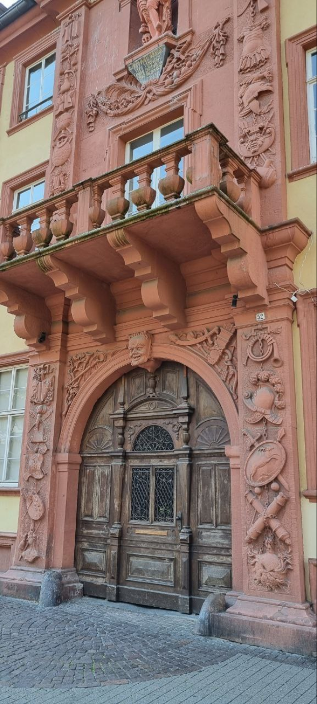 Altes Gebäude in der Heidelberger Altstadt mit einer hölzernen Tür, Fenstern und detaillierten Fassadenverzierungen.