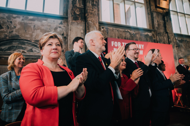 Eine Gruppe von Menschen, die vor einer Menge jubeln, mit einem Banner im Hintergrund, auf dem "Wahlsieg" steht.